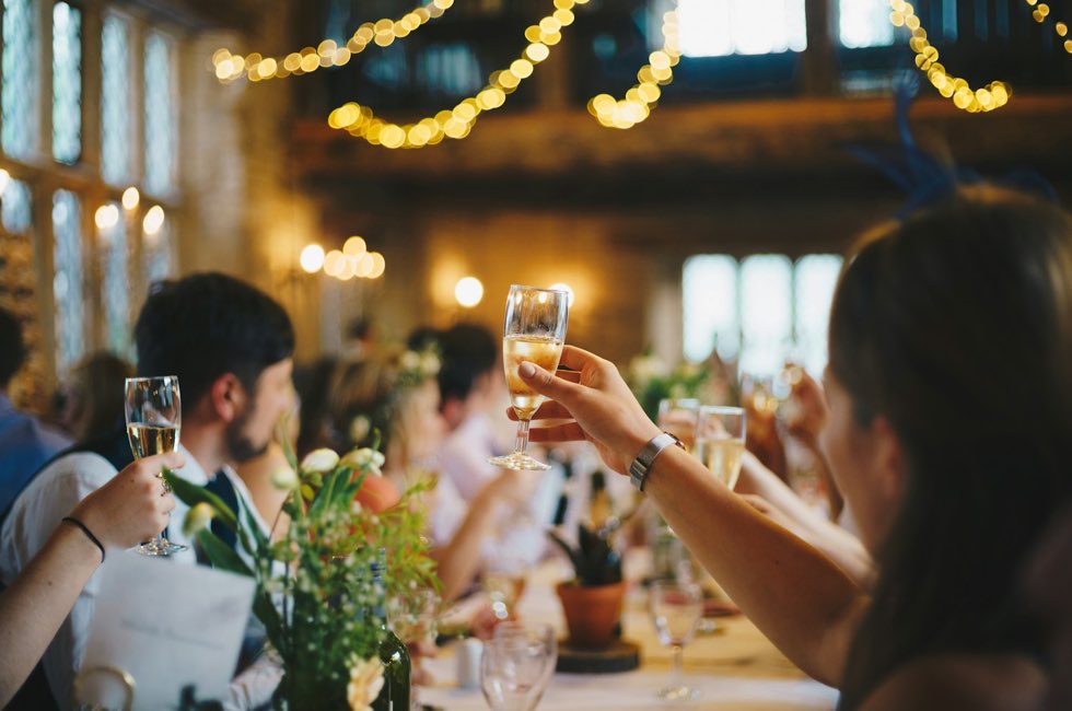 Invitados brindando con copas en una fiesta con luces colgantes