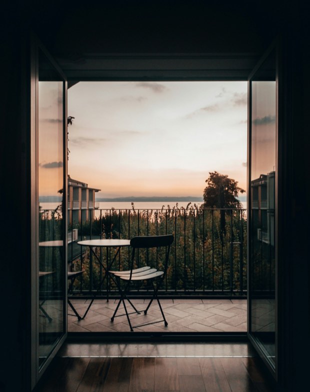 Puerta abierta a la galería de una habitación, con mesa y silla mirando al lago al atardecer