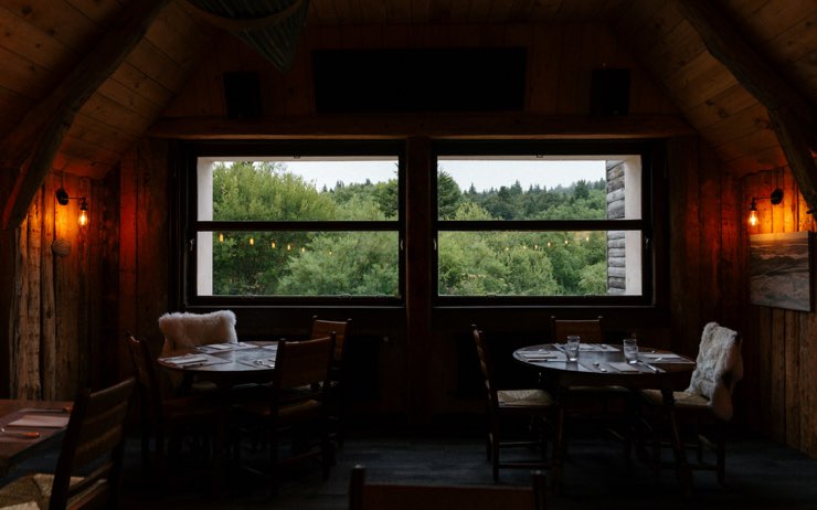 Comedor de madera con ventanales al bosque y mesas puestas