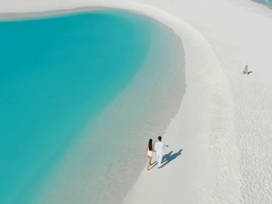 Banco de arena blanco y angosto rodeado de agua turquesa, con dos personas caminando