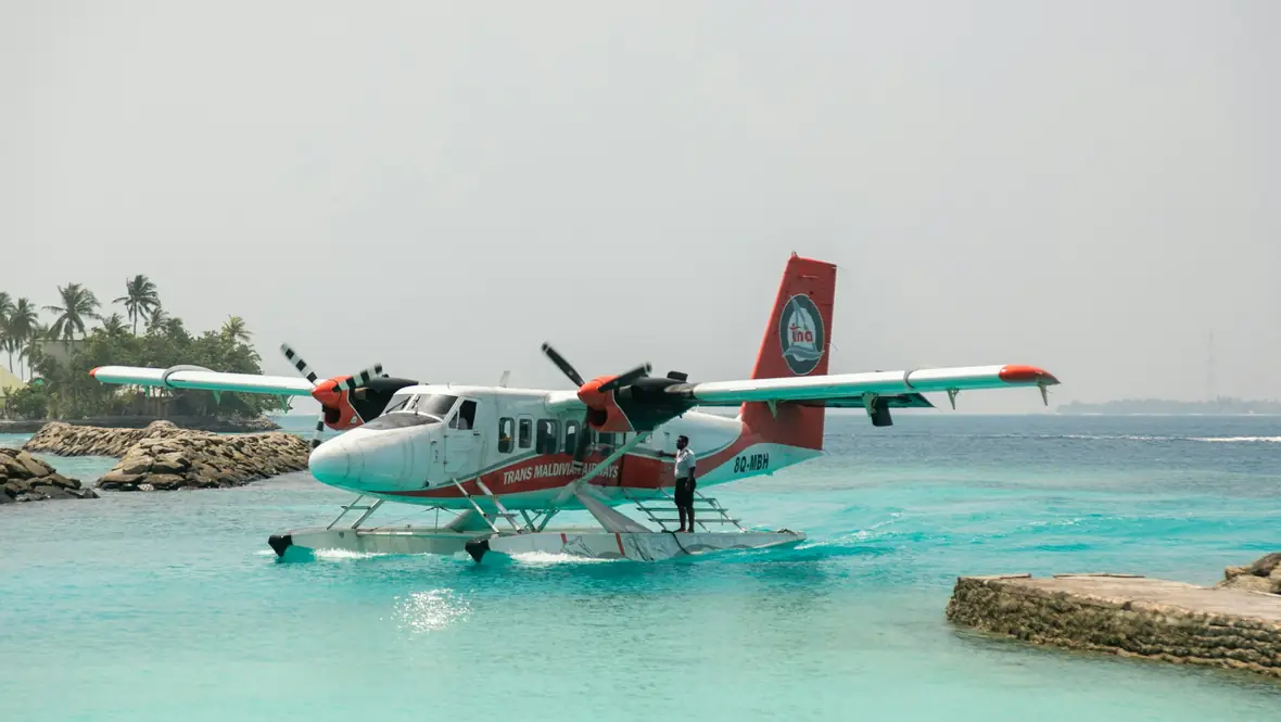 Hidroavión de hélices posado sobre agua turquesa junto a un muelle de piedra
