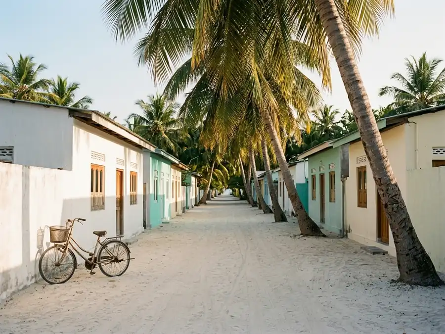Calle de arena de una isla tropical, con bicicletas apoyadas y casas bajas entre palmeras